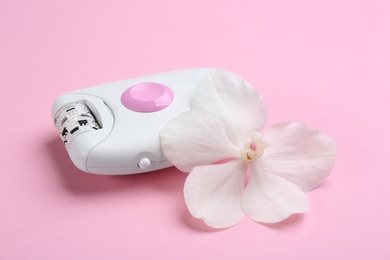 Photo of Modern epilator and flower on pink background