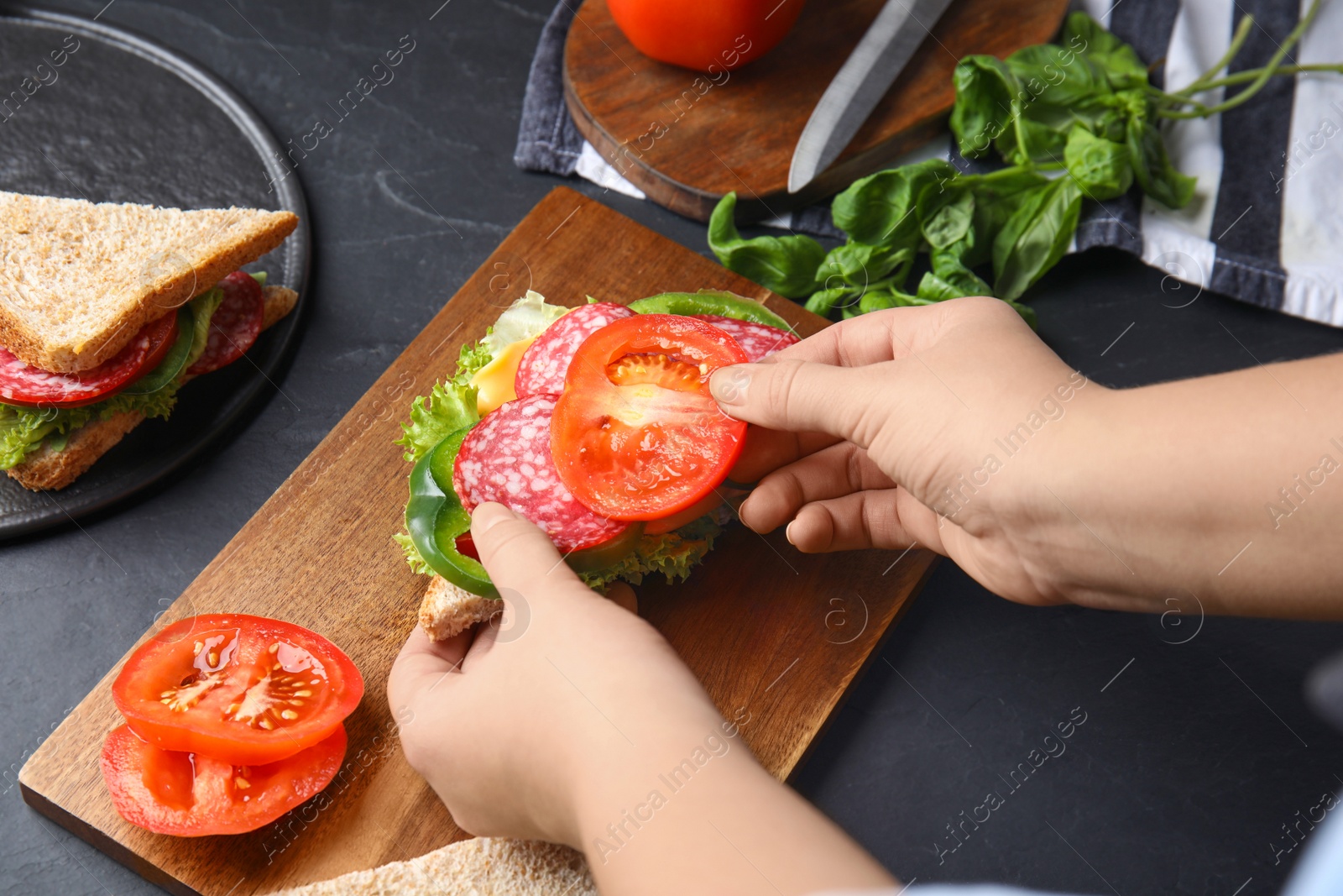 Photo of Woman adding tomato to sandwich at black table, closeup