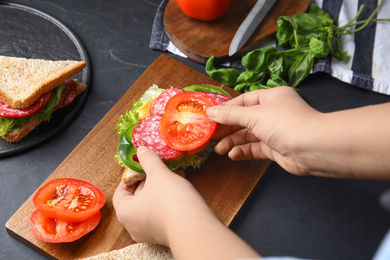 Photo of Woman adding tomato to sandwich at black table, closeup