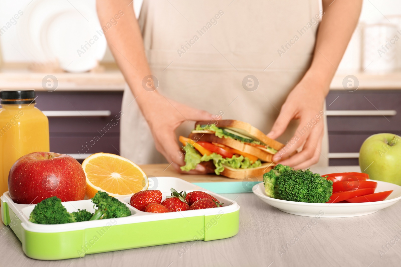 Photo of Woman preparing food for her child at table in kitchen, closeup. Healthy school lunch