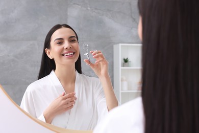 Beautiful young woman with eyelash curler near mirror in bathroom
