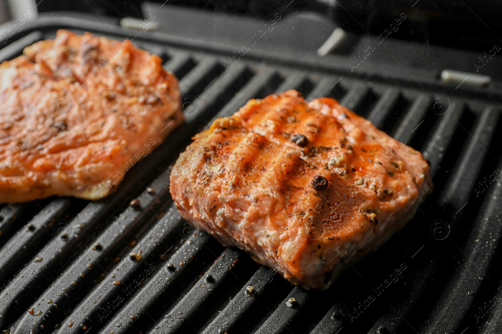 Photo of Tasty salmon cooking on electric grill, closeup