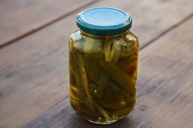 Glass jar of pickled green jalapeno peppers on wooden table, closeup