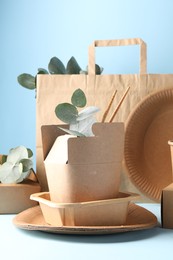 Photo of Eco friendly food packaging. Paper containers, tableware, bag and eucalyptus branches on white table against light blue background