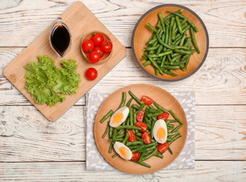 Photo of Flat lay composition with tasty green beans, eggs and  tomatoes on wooden table