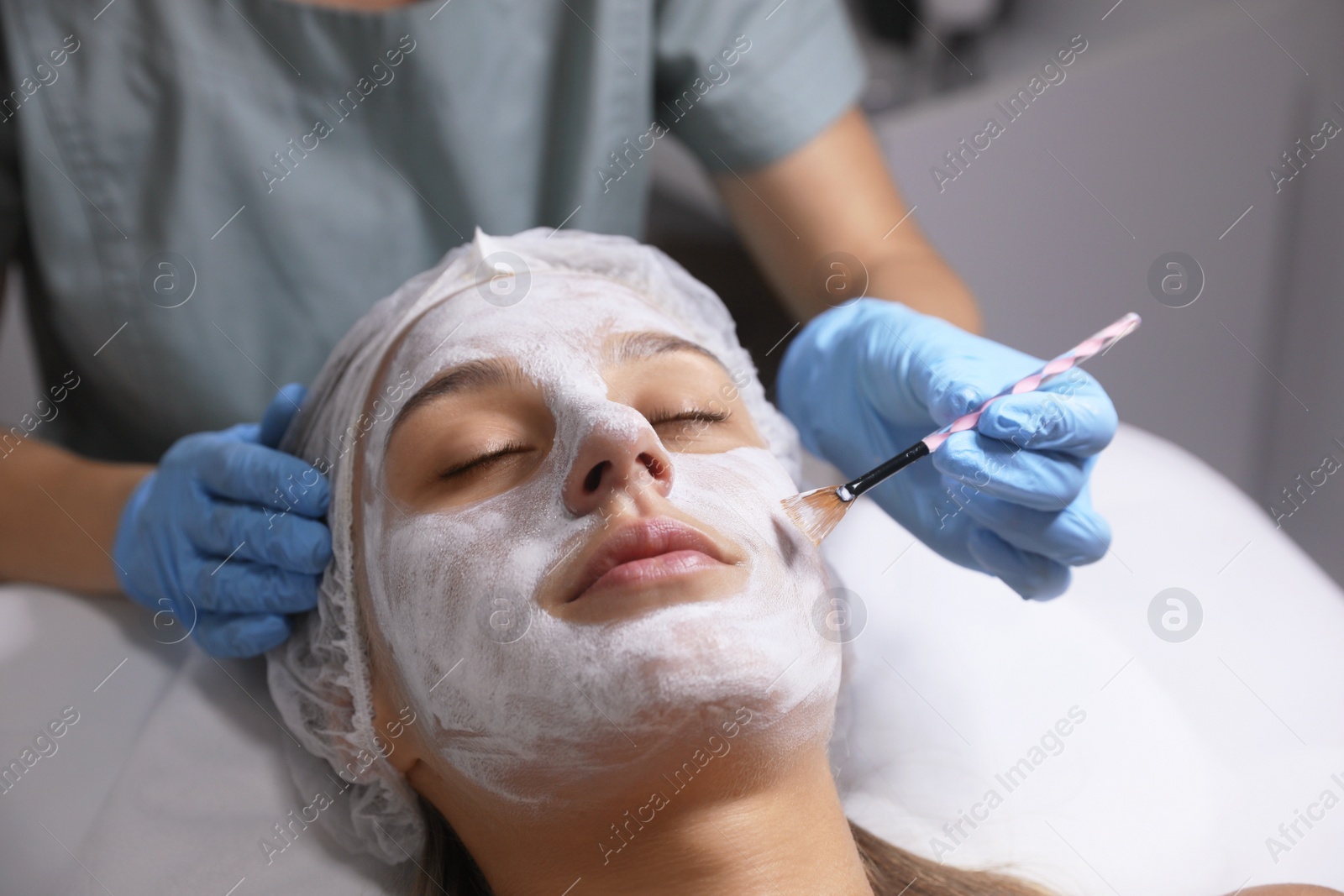 Photo of Cosmetologist applying mask on client's face in spa salon