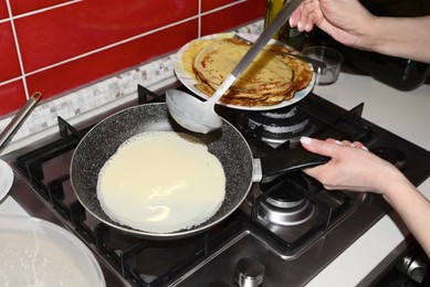 Photo of Woman pouring crepe batter onto frying pan in kitchen, closeup