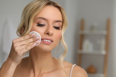 Beautiful woman removing makeup with cotton pad indoors. Space for text