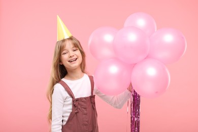 Photo of Happy little girl in party hat with bunch of balloons on pink background