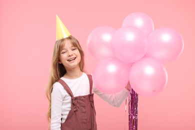 Happy little girl in party hat with bunch of balloons on pink background