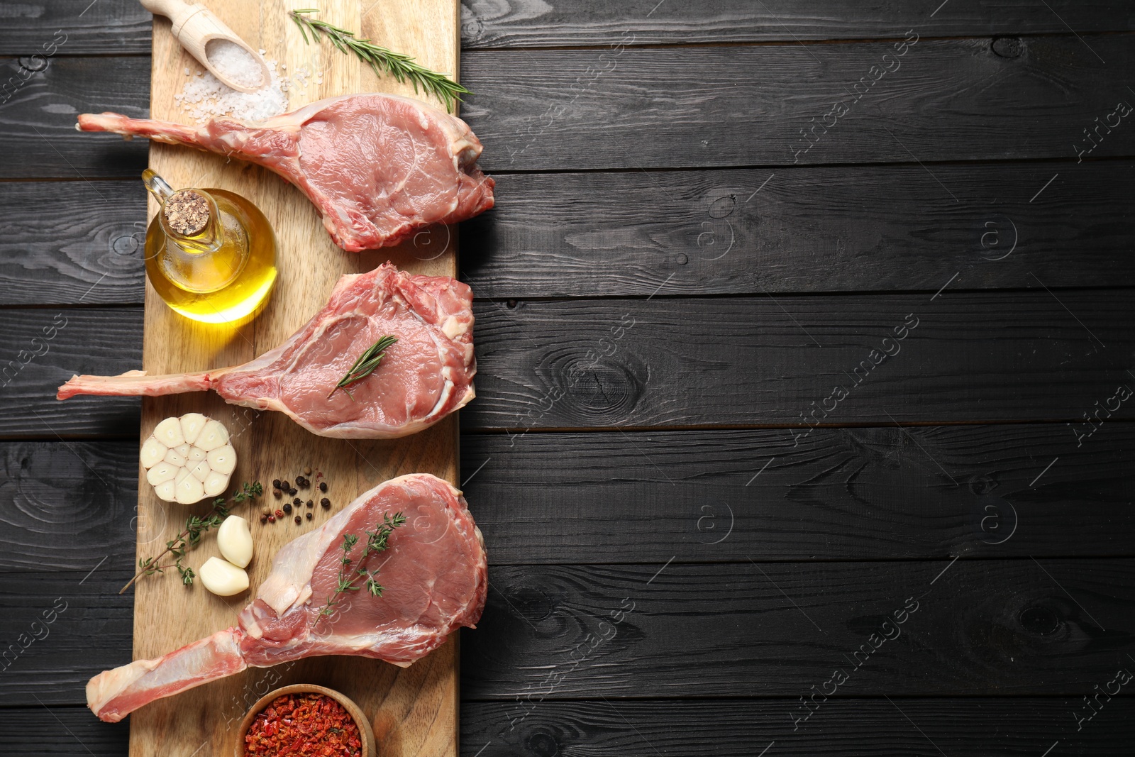 Photo of Fresh tomahawk beef cuts, spices and oil on black wooden table, top view. Space for text