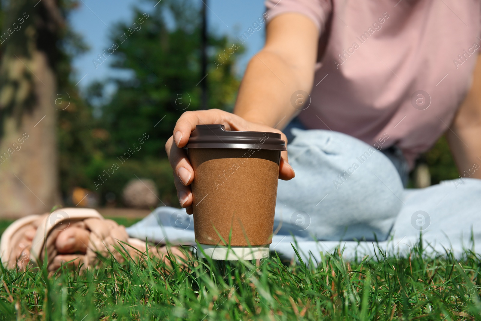 Photo of Woman holding takeaway cardboard coffee cup with plastic lid in park, closeup