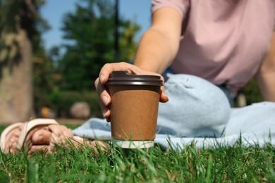 Photo of Woman holding takeaway cardboard coffee cup with plastic lid in park, closeup