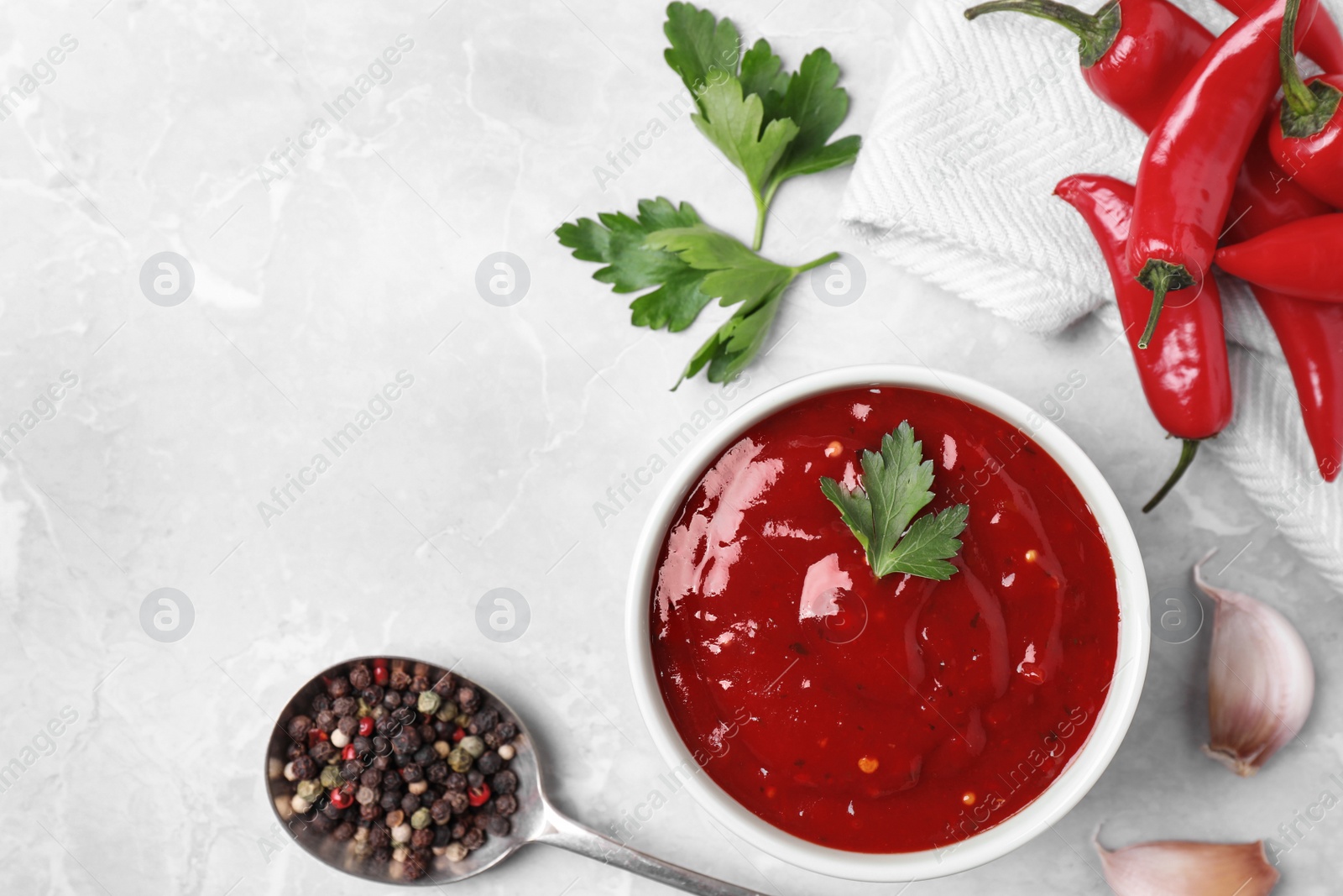 Photo of Bowl of hot chili sauce with ingredients on table, flat lay. Space for text