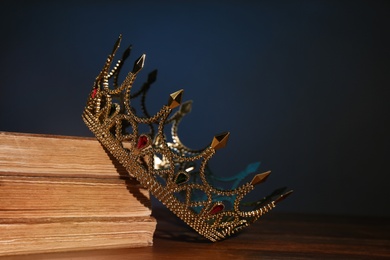 Photo of Beautiful golden crown and old books on wooden table. Fantasy item
