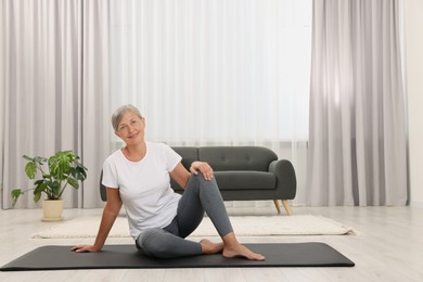 Happy senior woman sitting on mat at home, space for text. Yoga practice