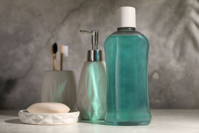 Bottle of mouthwash, toothbrushes and soap on light table in bathroom