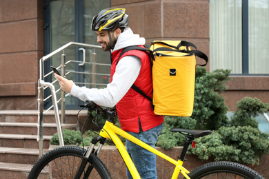 Photo of Courier with thermo bag, bicycle and mobile phone on city street. Food delivery service