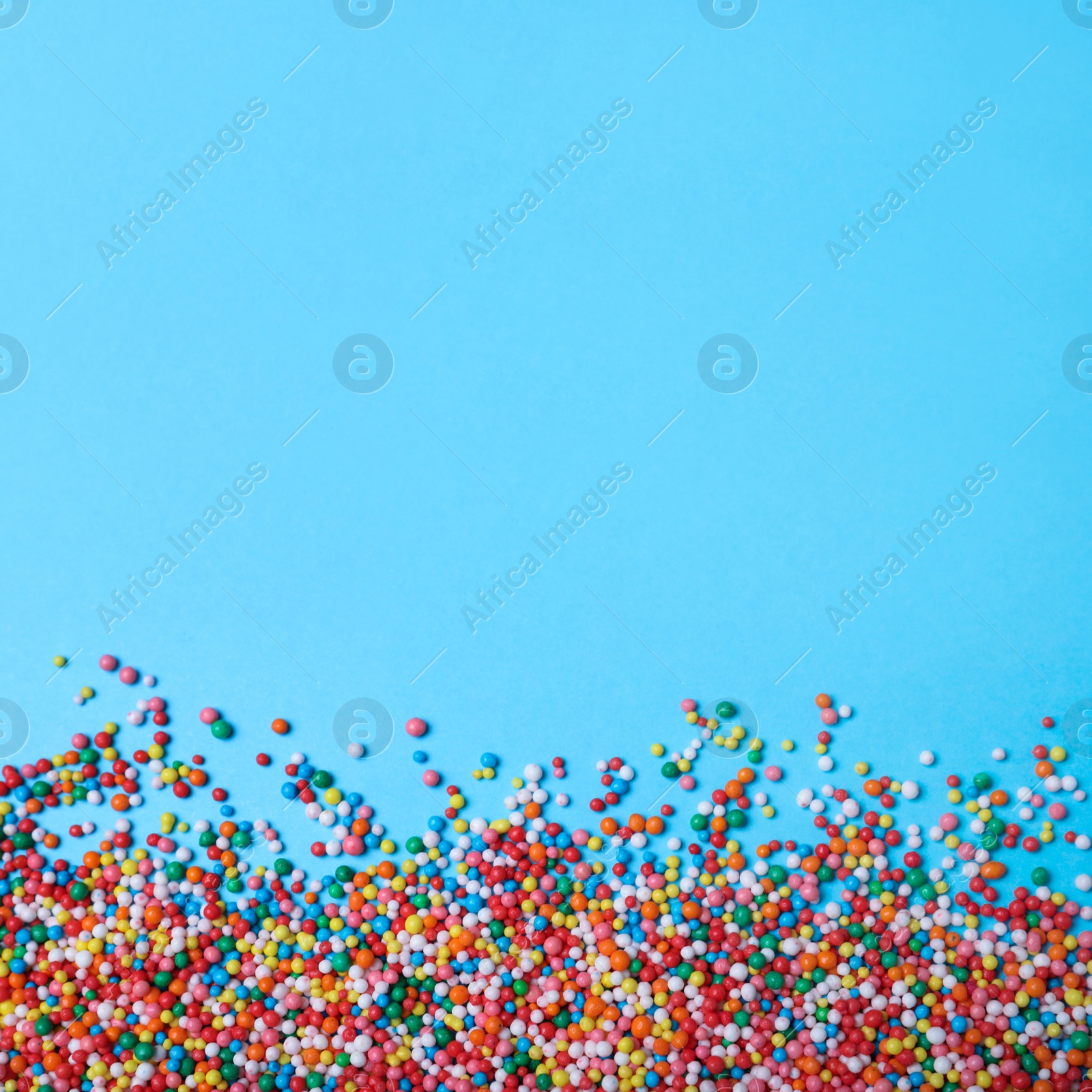 Photo of Colorful sprinkles on light blue background, flat lay with space for text. Confectionery decor