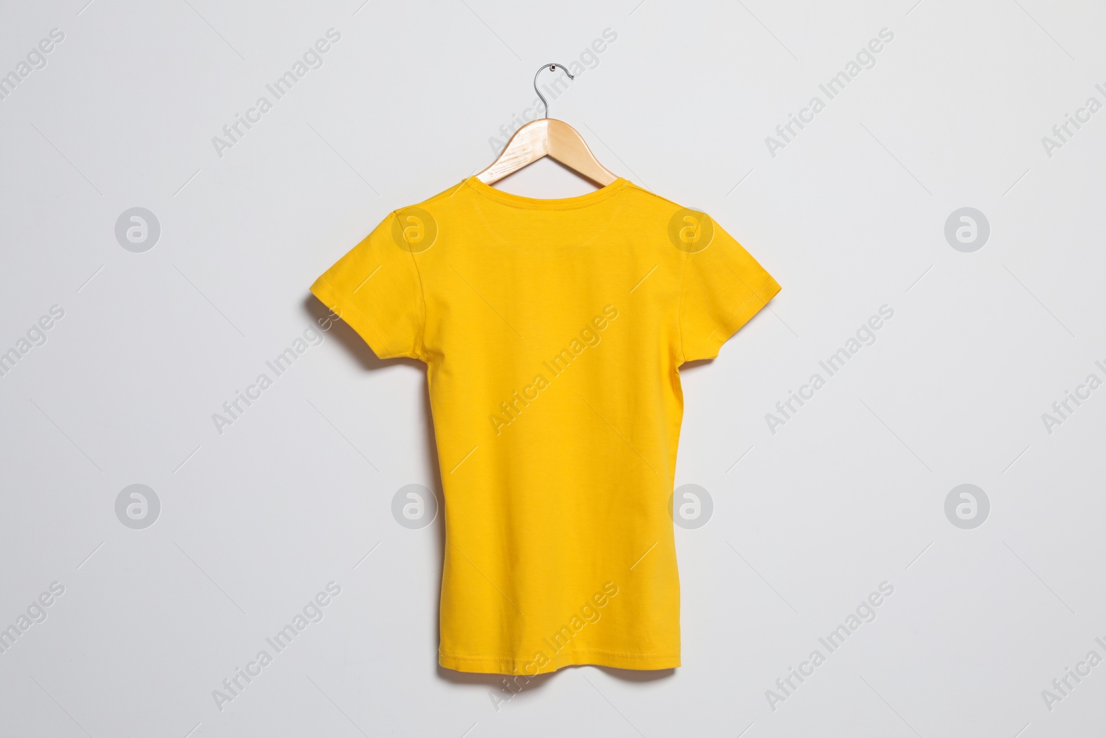 Photo of Hanger with yellow t-shirt on light wall. Mockup for design