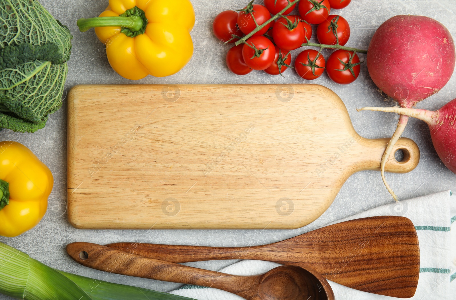 Photo of Wooden board surrounded by different fresh vegetables on grey table, flat lay with space for text. Cooking classes