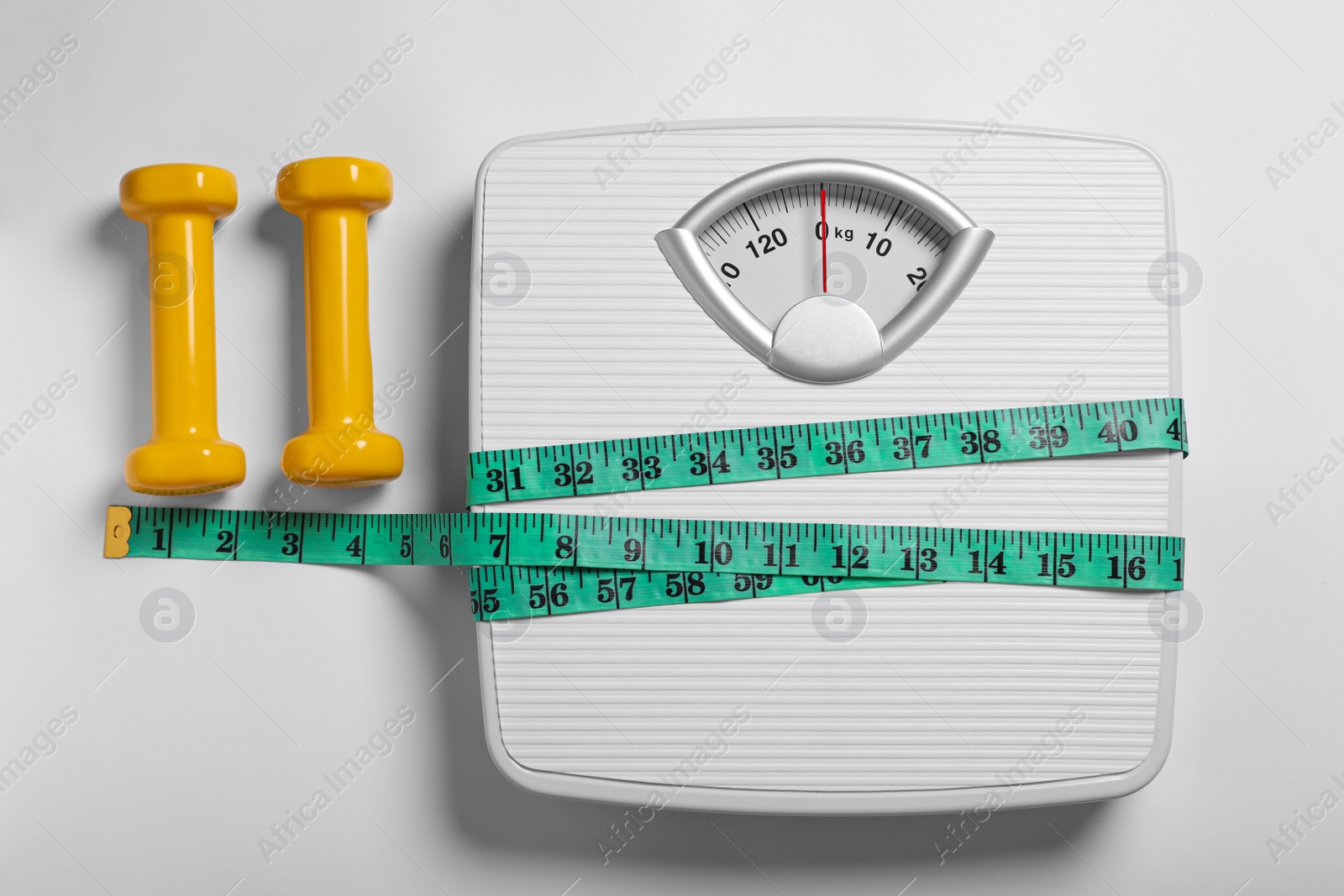 Photo of Weight loss concept. Scales, dumbbells and measuring tape on white background, flat lay
