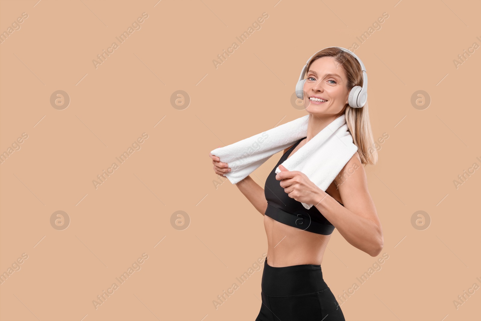 Photo of Athletic woman with headphones and white towel on beige background, space for text