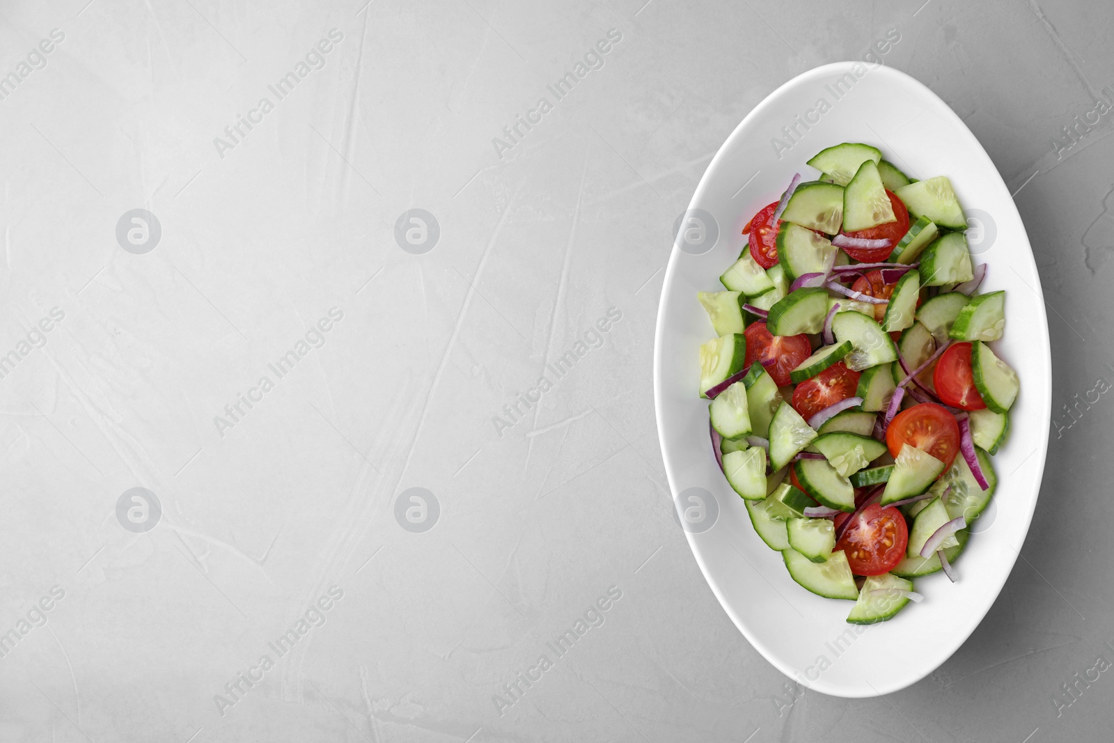 Photo of Plate of vegetarian salad with cucumber, tomato and onion on light background, top view. Space for text