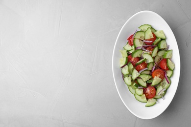 Plate of vegetarian salad with cucumber, tomato and onion on light background, top view. Space for text