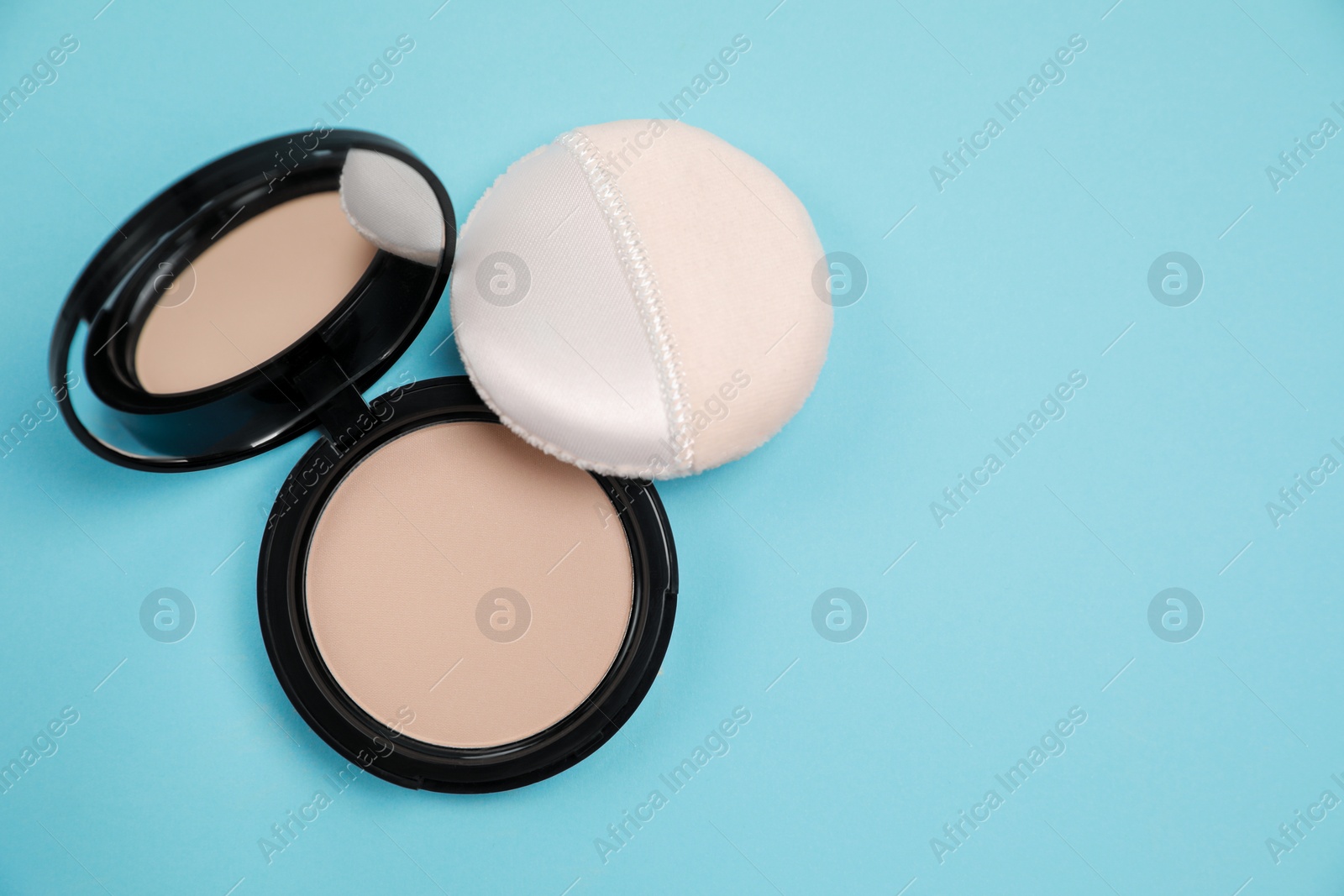 Photo of Face powder and puff on light blue background, flat lay. Space for text