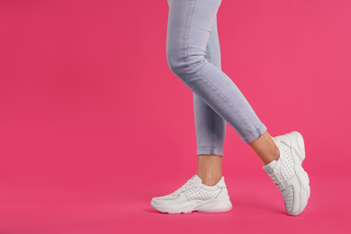 Photo of Woman wearing sneakers on pink background, closeup. Space for text