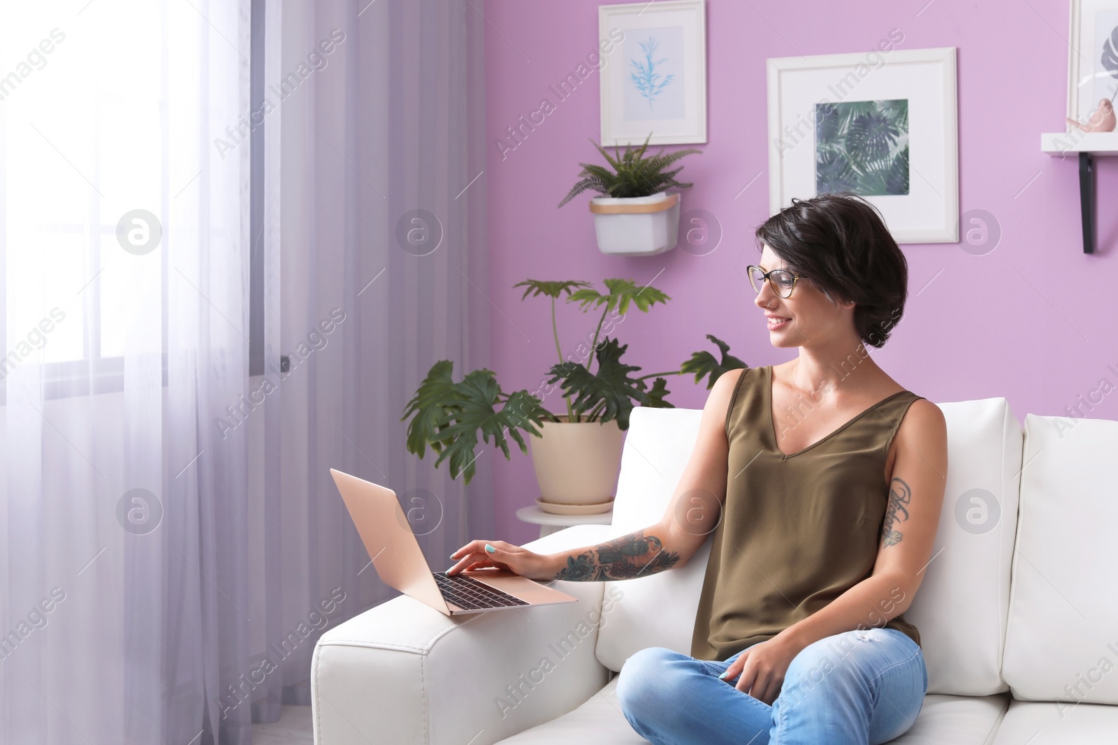 Photo of Young woman with modern laptop sitting on sofa at home