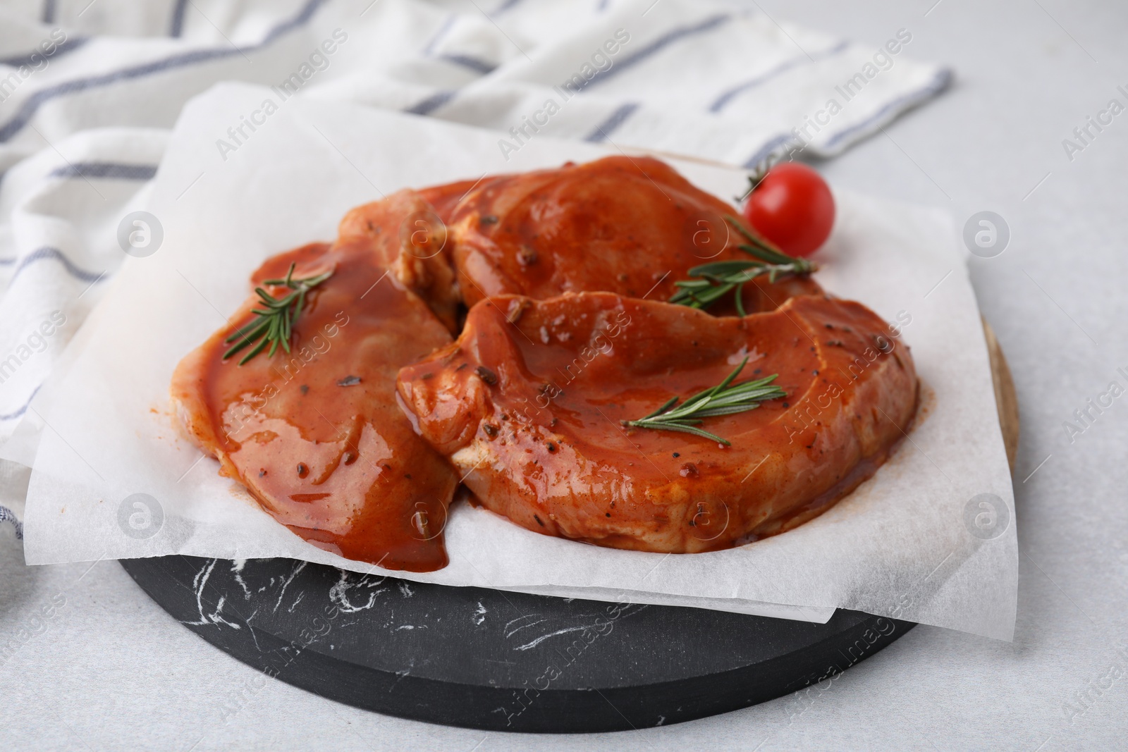 Photo of Board with raw marinated meat, rosemary and tomato on light table, closeup