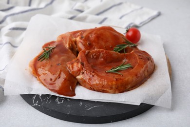 Board with raw marinated meat, rosemary and tomato on light table, closeup