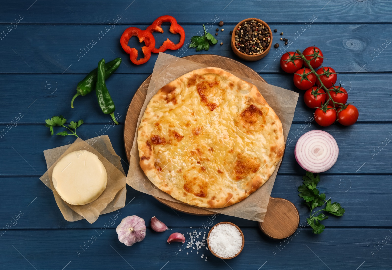 Photo of Delicious khachapuri, cheese, vegetables and spices on blue wooden table, flat lay