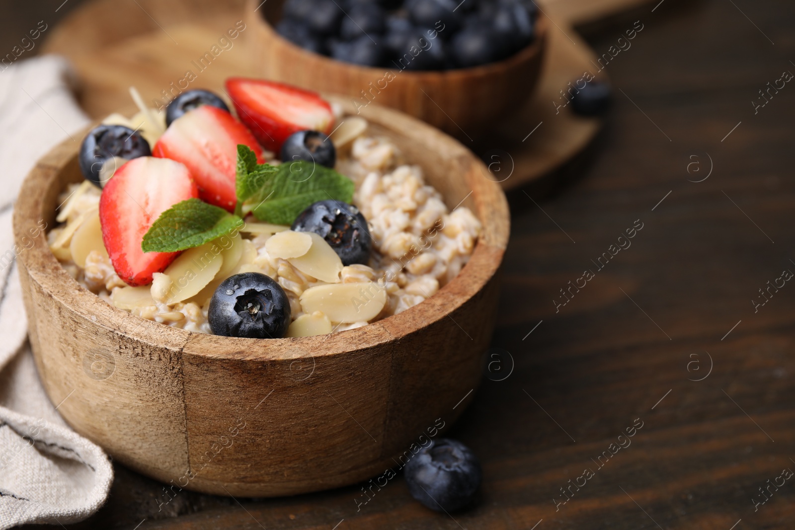 Photo of Tasty oatmeal with strawberries, blueberries and almond flakes in bowl on wooden table, closeup. Space for text