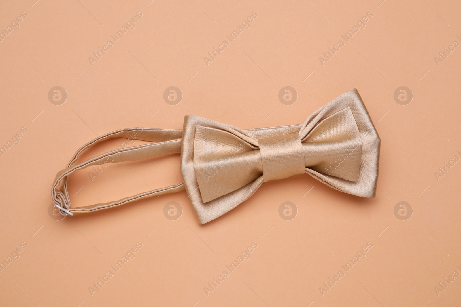 Photo of Stylish beige bow tie on pale orange background, top view