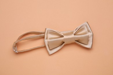 Stylish beige bow tie on pale orange background, top view