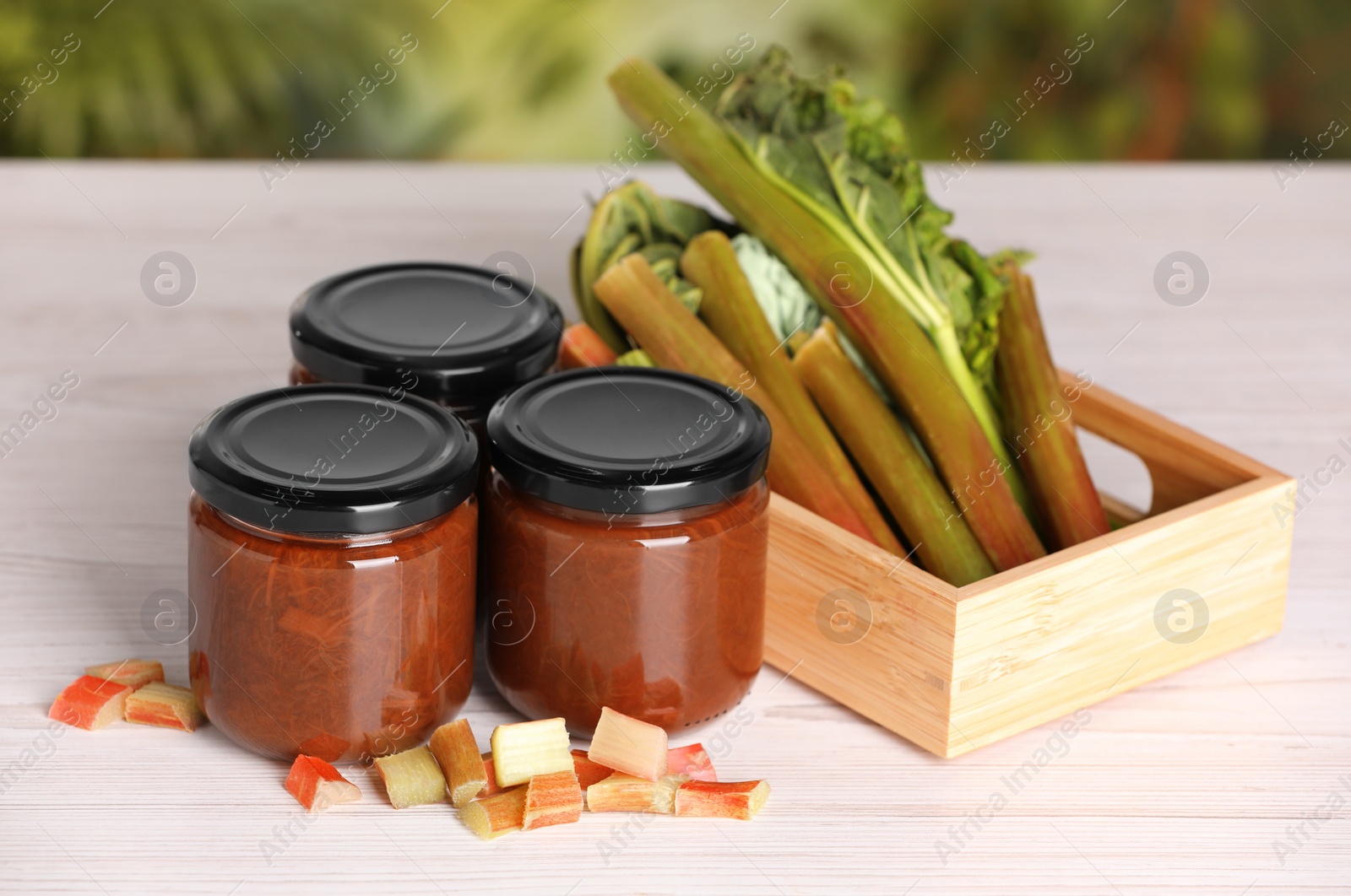 Photo of Jars of tasty rhubarb jam and stalks on white wooden table