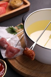 Photo of Fondue pot, forks with meat pieces and other products on black textured table, closeup