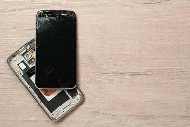 Photo of Damaged smartphone on wooden table, flat lay with space for text. Device repairing