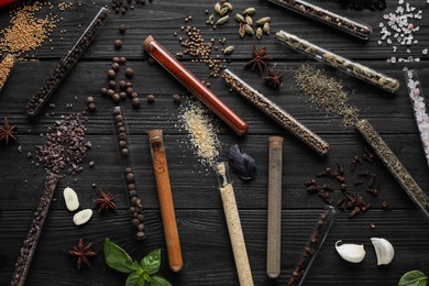 Photo of Flat lay composition with various spices, test tubes and fresh herbs on black wooden background