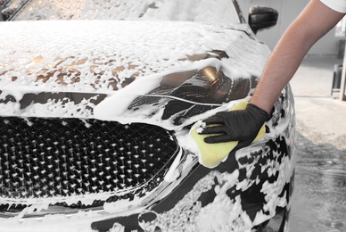 Photo of Young worker cleaning automobile with sponge at car wash, closeup