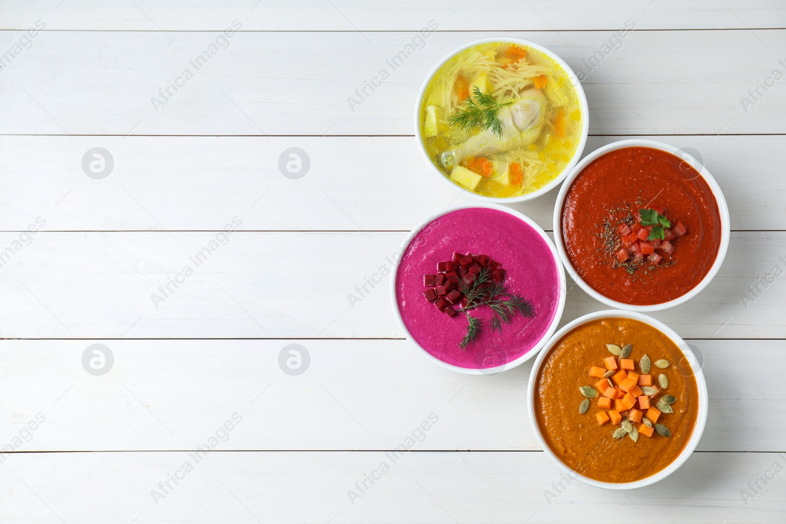 Photo of Tasty broth and different cream soups in bowls on white wooden table, flat lay. Space for text