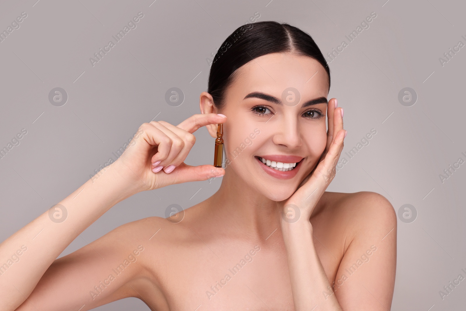 Photo of Beautiful young woman holding skincare ampoule on grey background