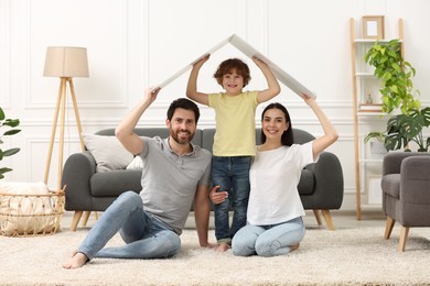 Photo of Housing concept. Happy family holding plastic roof on floor at home