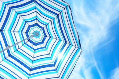 Image of Open big striped beach umbrella and beautiful blue sky with white clouds on background