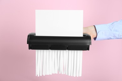 Photo of Woman destroying sheet of paper with shredder on pink background, closeup