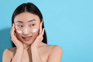 Photo of Beautiful young woman with sun protection cream on her face against light blue background, space for text