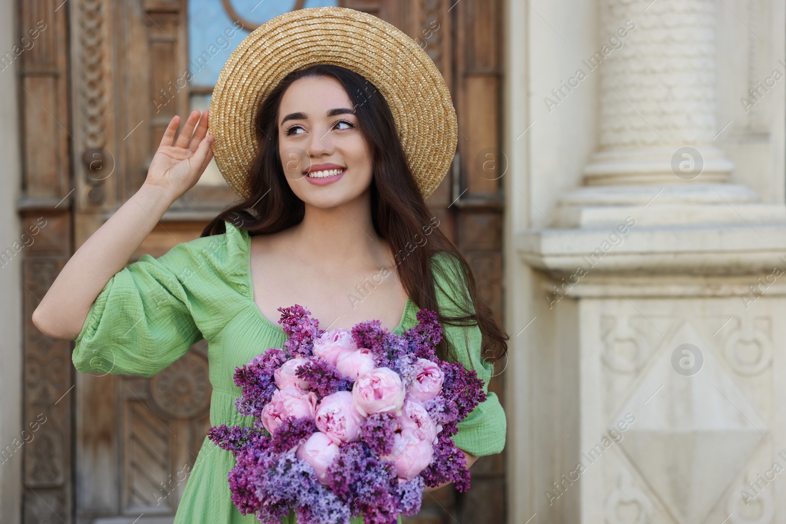 Photo of Beautiful woman with bouquet of spring flowers near building outdoors, space for text